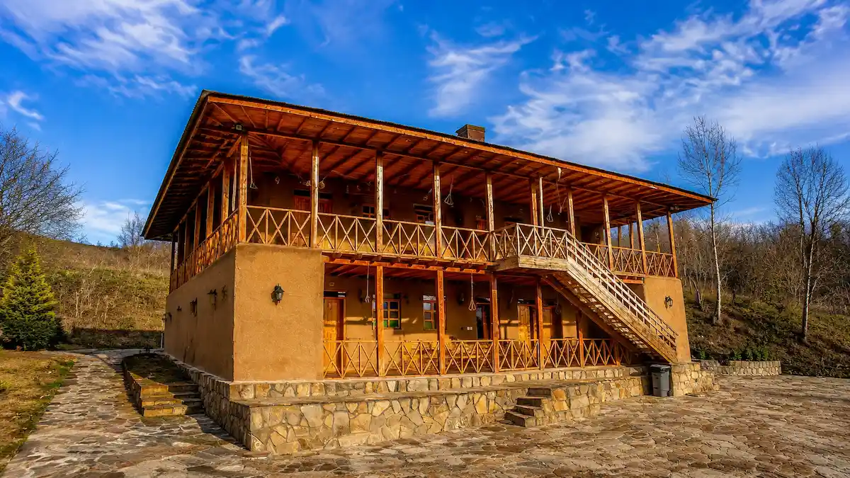 اقامتگاه بوم‌گردی در رودبار با معماری سنتی، ایوان چوبی، چشم‌انداز کوهستان و فضای روستایی در میان طبیعت گیلان.