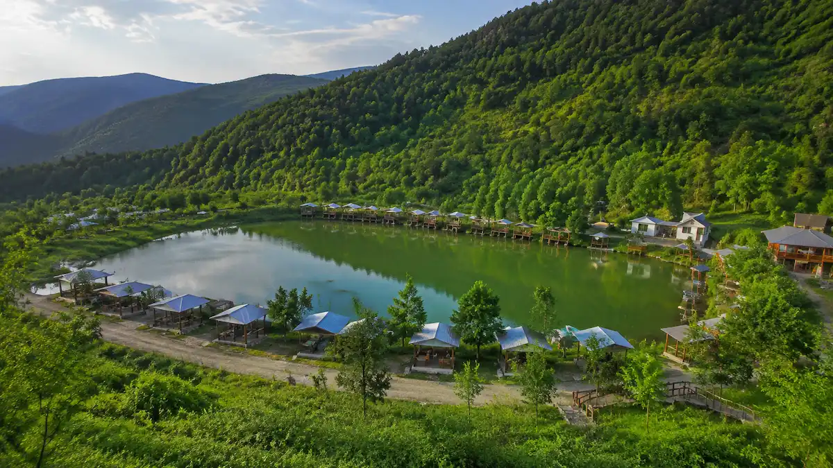 چشم‌انداز طبیعی رستم آباد در استان گیلان با جنگل‌های انبوه، رودخانه و خانه‌های روستایی سنتی در دامنه کوه‌های البرز